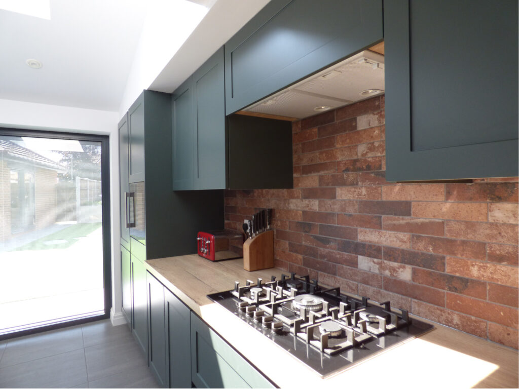 A green handleless Kitchen with brass rails. A wood worktop runs along the back bank with a hob built in.